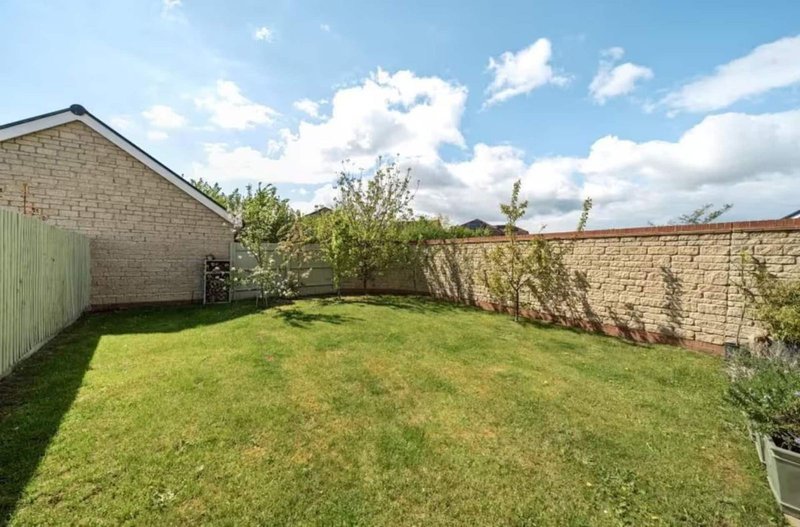 Spacious garden with green lawn, brick walls, shed and blue sky