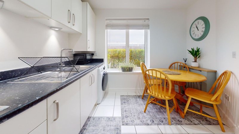Modern kitchen with white cabinets, dark countertop, dining area with wooden chairs and window view