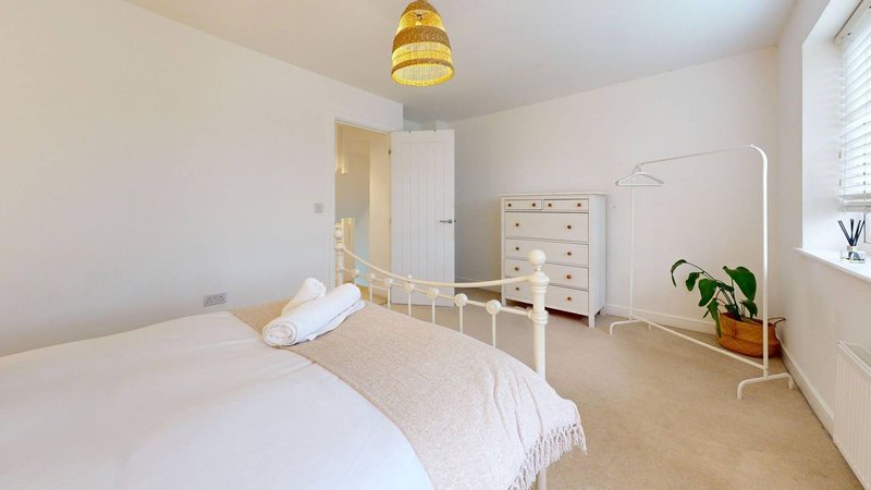 Bright bedroom with white metal bed frame, chest of drawers, pendant light and potted plant