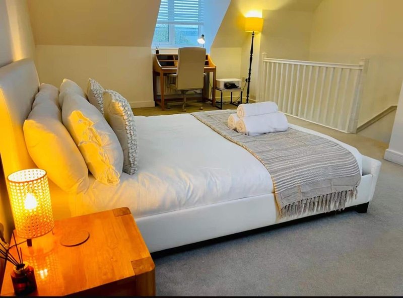 Spacious bedroom with double bed, decorative pillows, yellow accent lighting, and sloped ceiling