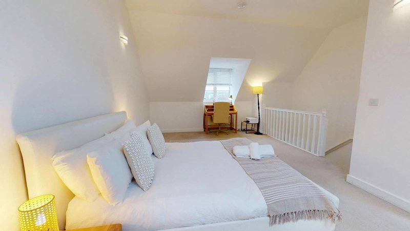 Bright attic bedroom with double bed, white bedding, skylight window and radiator