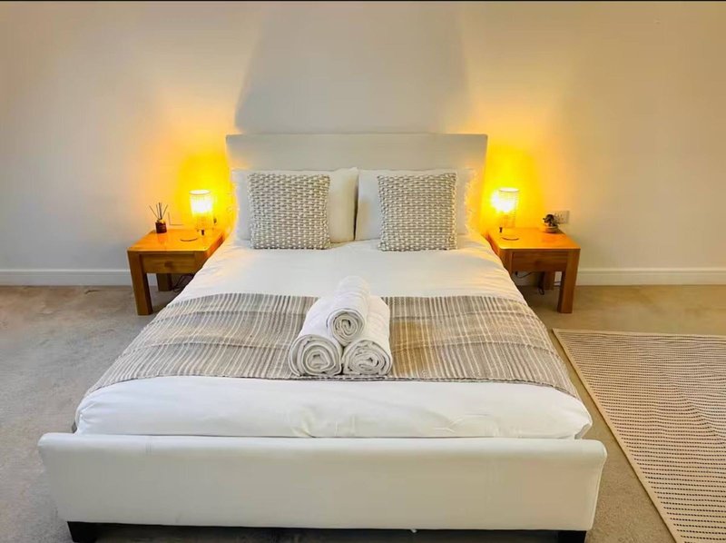 Modern bedroom with white bed, two wooden nightstands, yellow lamps, and neutral decor