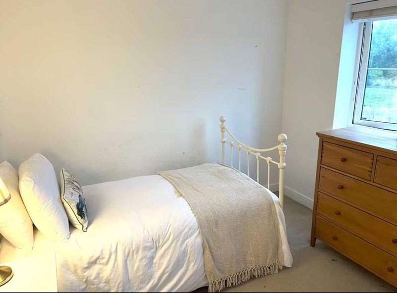 Bright bedroom with single bed, brass headboard, wooden chest of drawers, and window view
