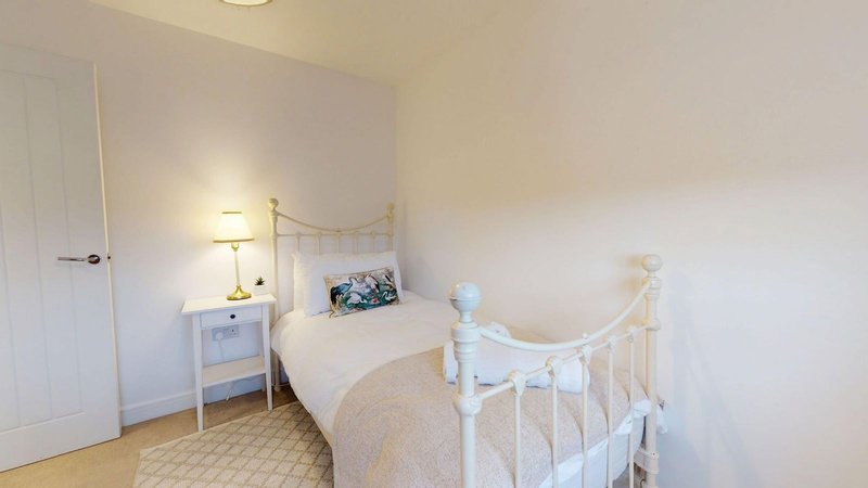 Bright bedroom with white metal bed frame, bedside tables with lamps, and cream carpeting