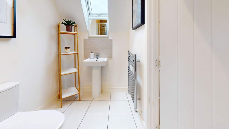 Clean white bathroom with pedestal sink, toilet, wooden plant shelf and tiled floor