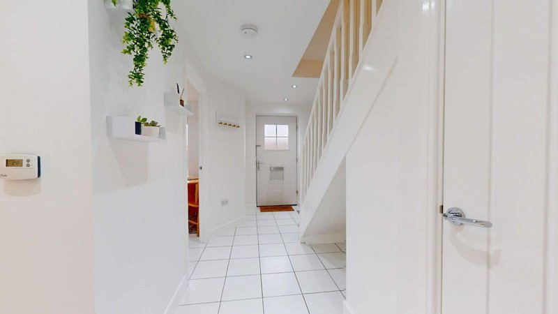 Bright hallway with white walls, tiled floor, staircase and hanging plant decoration