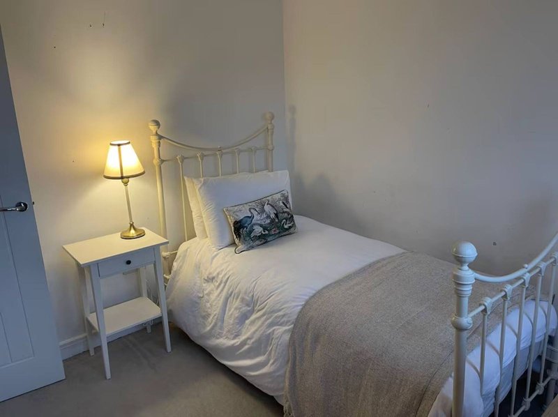 Bright bedroom with single bed, white metal frame, bedside lamp and small table