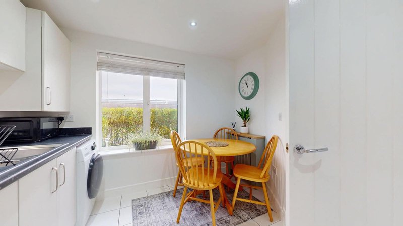 Modern kitchen with white cabinets, dining table, wooden chairs and garden view