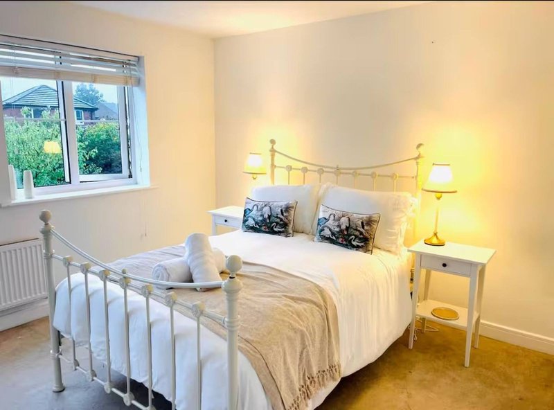 Bright bedroom with metal bed frame, white bedding, two nightstands with lamps and window view