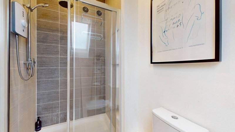 Modern bathroom with walk-in shower, white toilet, and framed line artwork on wall