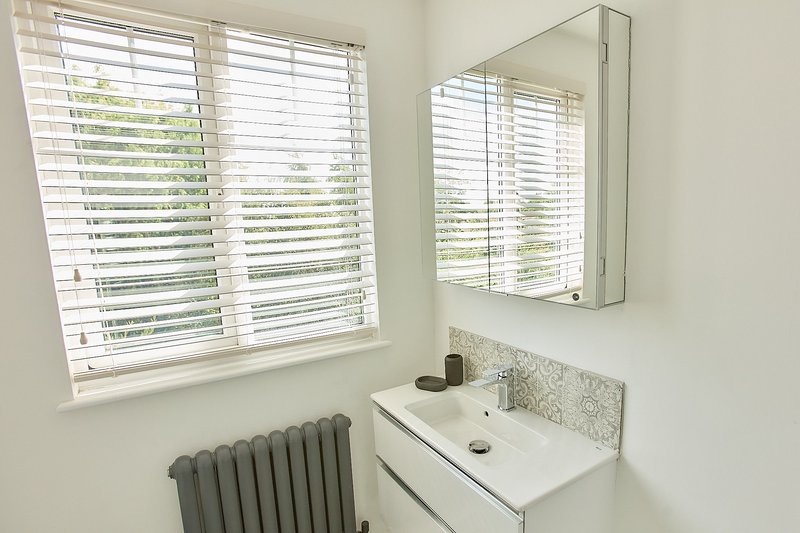 Clean modern bathroom with white sink, mirror cabinet, window with shutters, and radiator