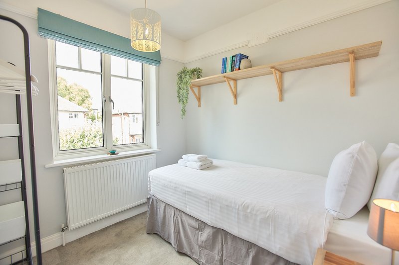 Bright bedroom with double bed, wooden shelves, window with teal valance and pendant light