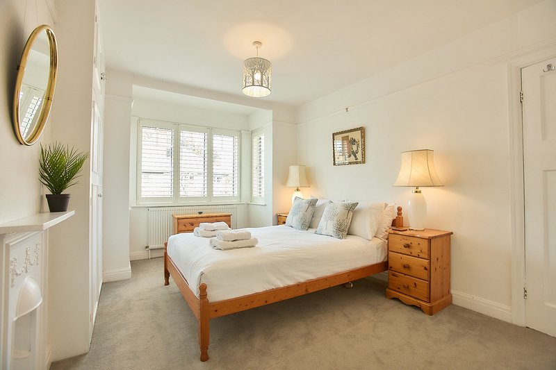 Bright bedroom with double bed, wooden frame, bedside tables, lamps and shuttered window