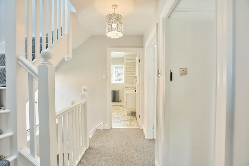 Bright hallway with staircase, white railings, pendant light and cream carpet