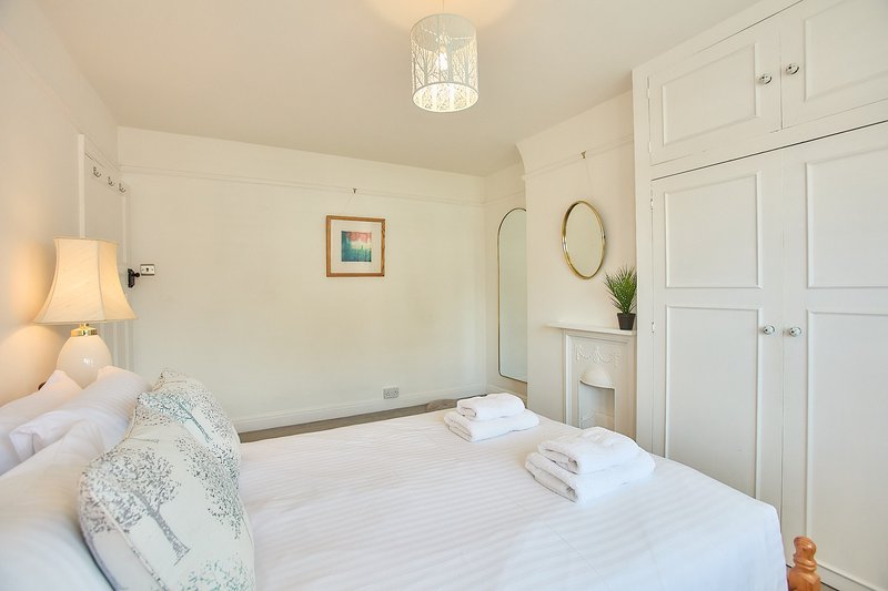Bright bedroom with double bed, white wardrobes, bedside lamp and framed wall art