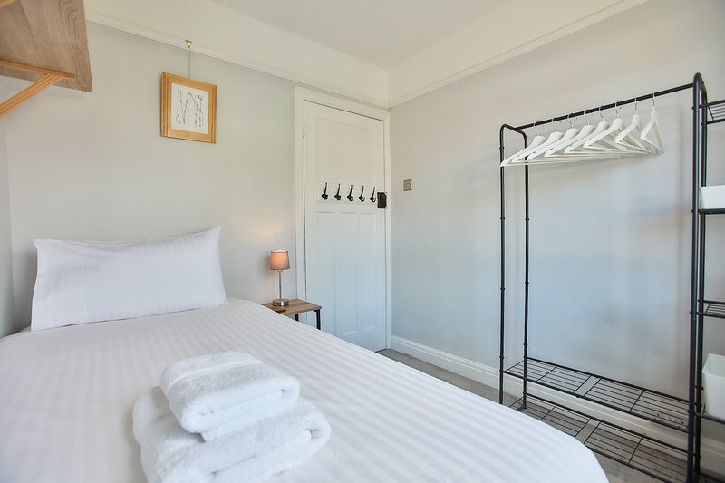 Clean bedroom with single bed, white bedding, towels, bedside lamp and clothes rack