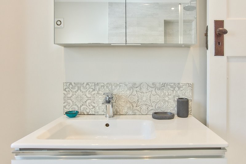 Modern bathroom sink with patterned tile backsplash, mirror cabinet and toiletries