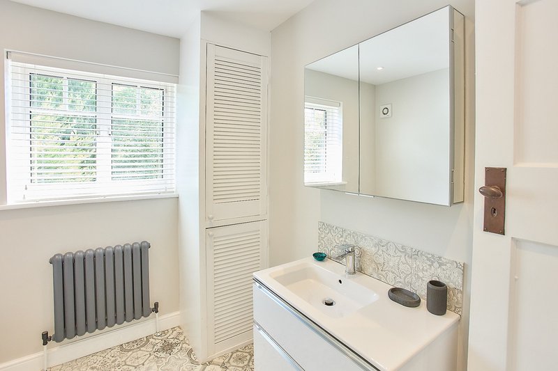 Bright modern bathroom with double sink, mirrored cabinet, radiator and window