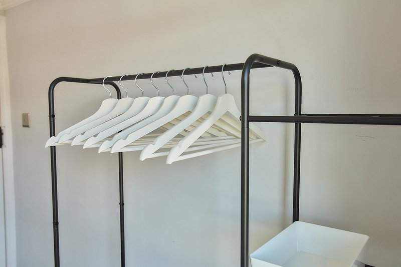 Black metal clothing rail with white wooden hangers in bright minimalist room