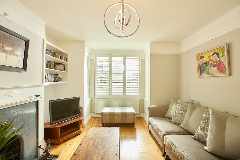 Bright living room with sofa, fireplace, TV stand, shelving and shuttered windows