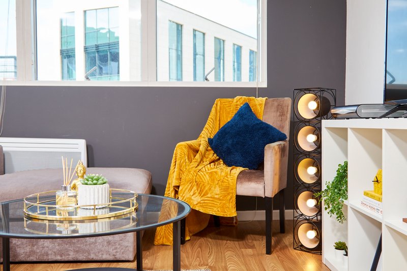 Modern living room with armchair, yellow throw blanket, blue cushion, round glass table and shelving