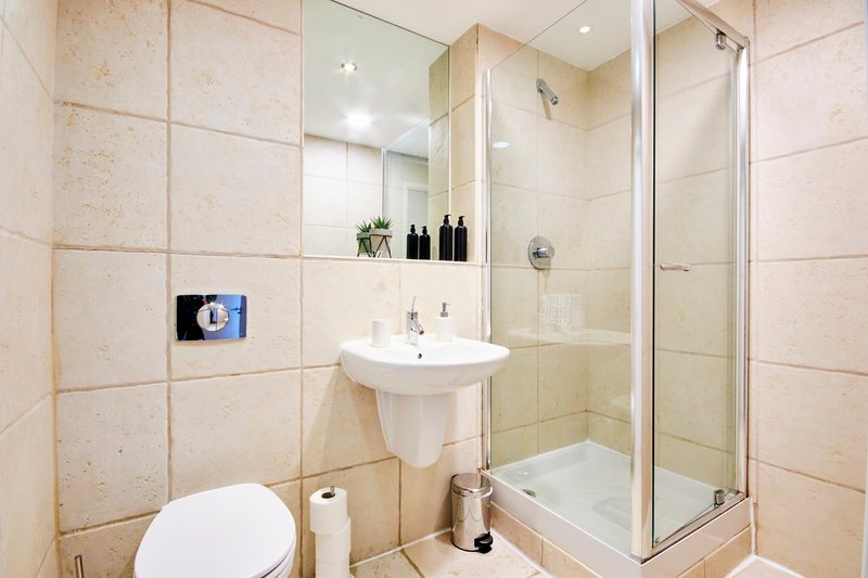 Modern bathroom with pedestal sink, toilet, shower enclosure and beige wall tiles