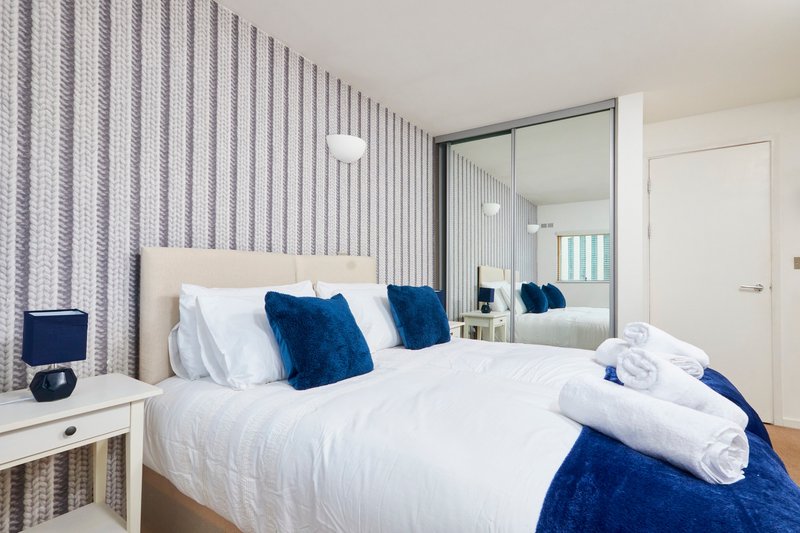 Modern bedroom with white bed, blue cushions, striped wallpaper and mirrored wardrobe