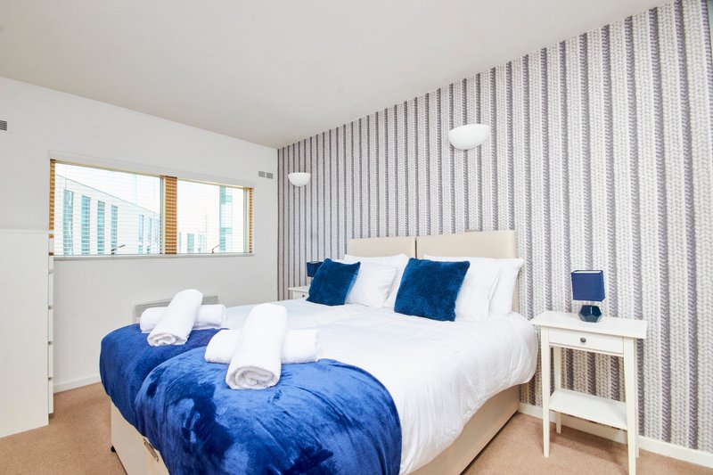 Modern bedroom with double bed, blue bedding, white pillows, striped wallpaper and wooden flooring