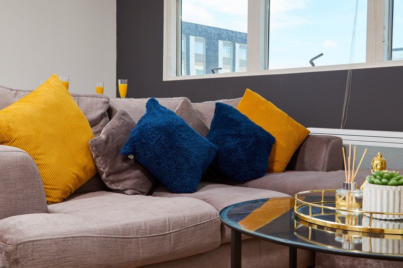 Modern living room with gray sofa, yellow and blue cushions, glass coffee table and city view