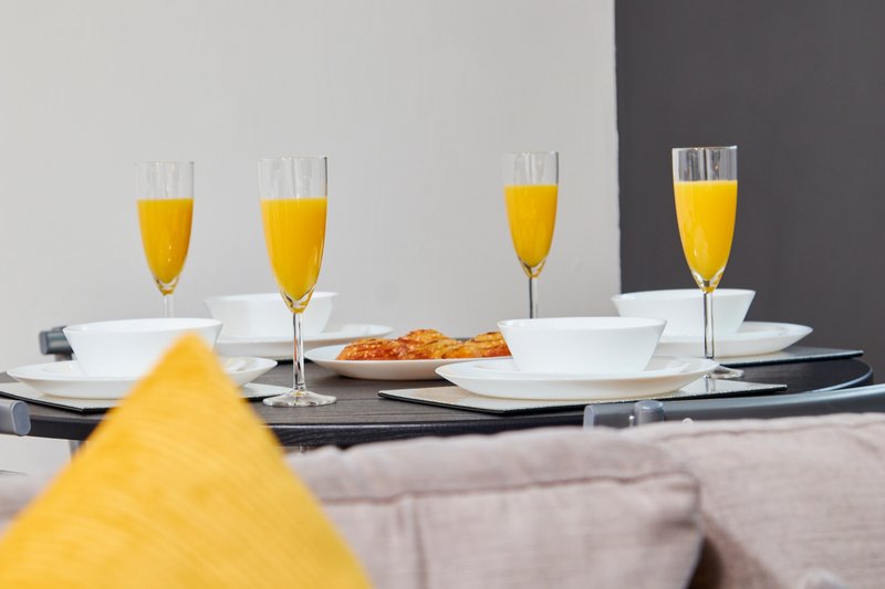 Dining table set with glasses of orange juice, white plates, and yellow napkin
