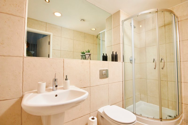 Modern bathroom with pink tiles, curved sink, mirror, toilet and shower cubicle