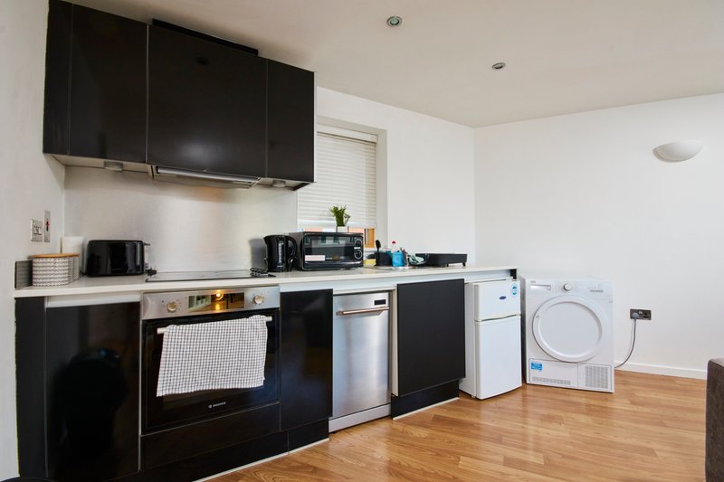 Modern kitchen with black cabinets, stainless steel appliances, white countertop and wooden flooring