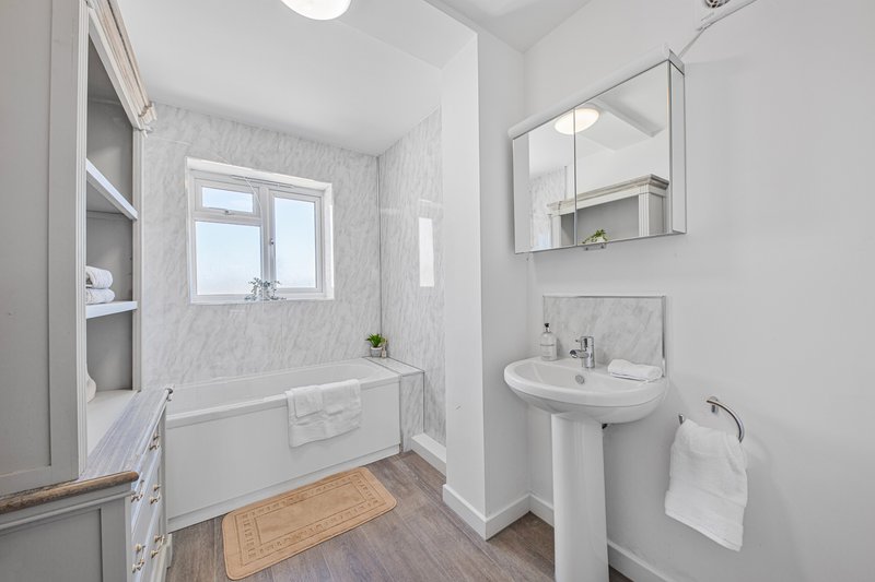 Modern bathroom with white tiles, pedestal sink, bathtub and wooden floor