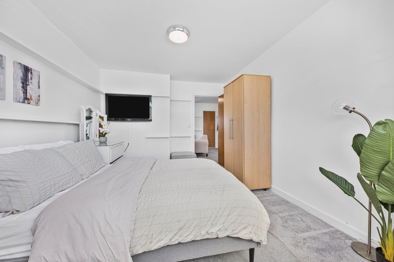 Modern bedroom with double bed, wooden wardrobe, wall-mounted TV and potted plant
