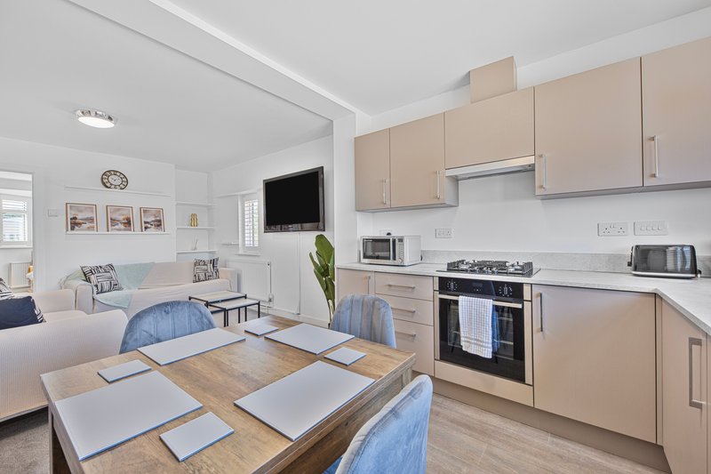 Modern open-plan kitchen and dining area with wooden table, blue chairs, and beige cabinetry