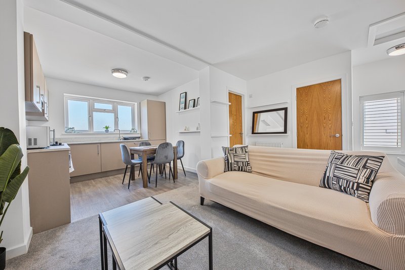 Open-plan living room with cream sofa, dining table, chairs and kitchen area visible