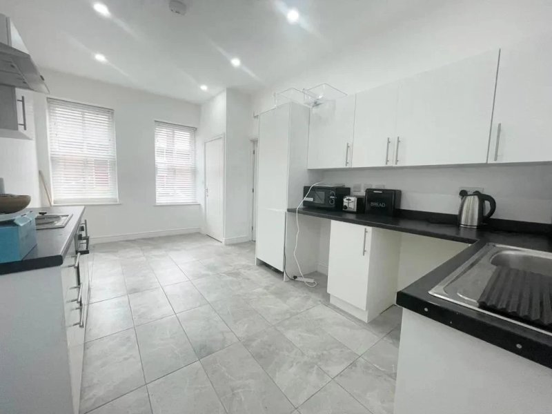 Modern kitchen with white cabinetry, black countertops, stainless steel appliances and tiled flooring