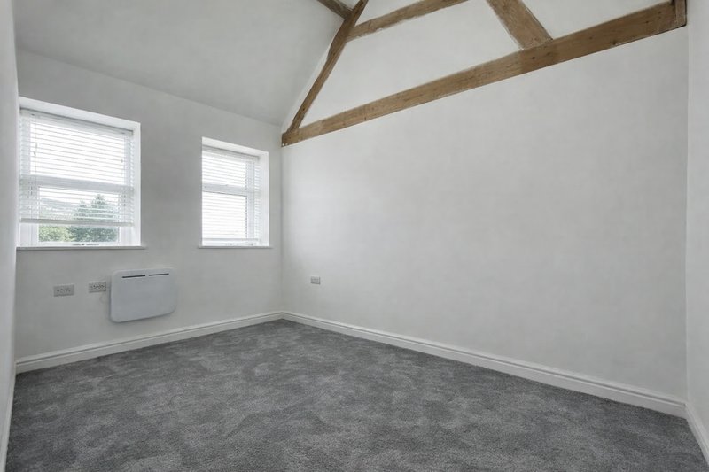 Empty bedroom with exposed wooden beams, two windows, radiator and grey carpeted floor