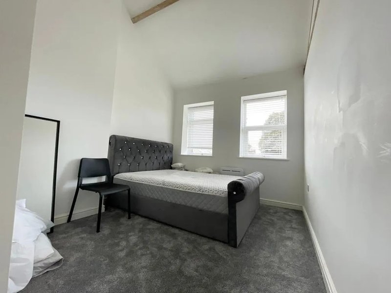 Bedroom with double bed, black chair, grey carpet and two windows