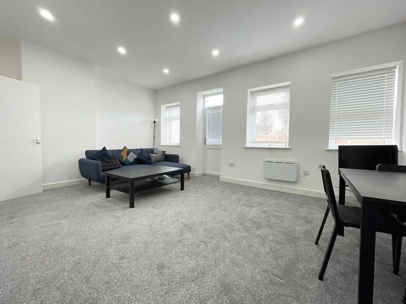Modern open-plan living room with grey carpet, navy sofa, black coffee table and dining area