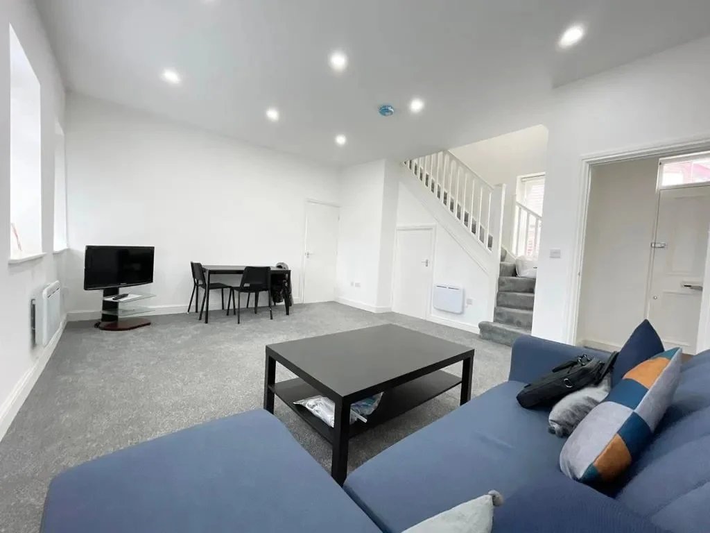 Open-plan living room with blue sofa, black coffee table, dining area and staircase