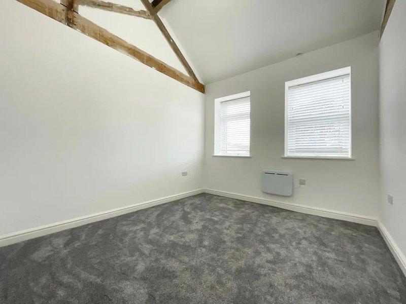 Empty bedroom with grey carpet, exposed wooden beams, white walls and two windows
