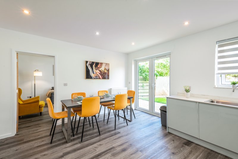 Modern open-plan dining and kitchen area with yellow chairs, dining table, and view to garden