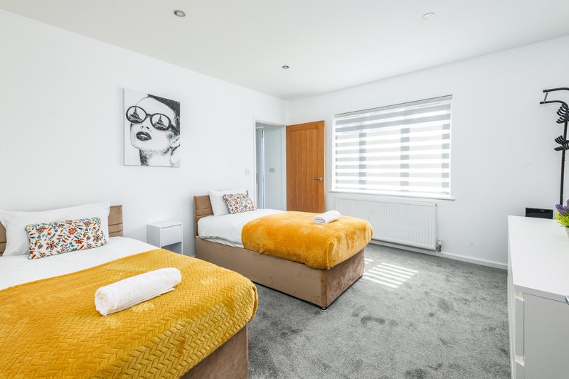Bright modern bedroom with two beds, mustard yellow bedding, white walls and grey flooring