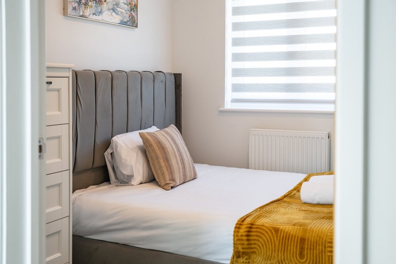 Bedroom with single bed, grey upholstered headboard, striped pillows and yellow throw blanket