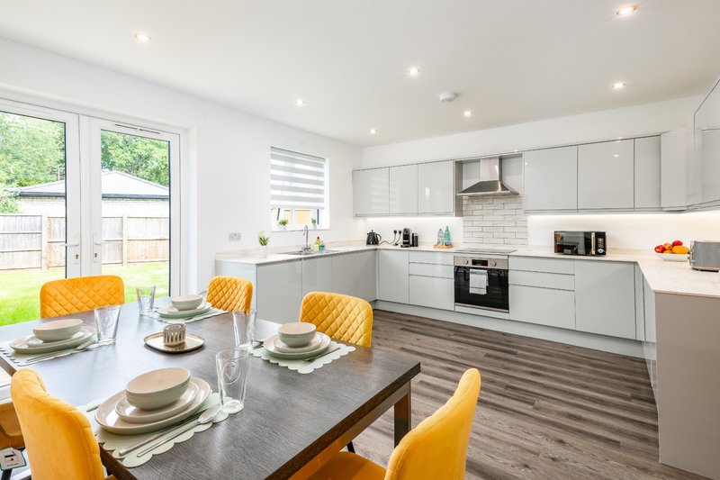 Modern kitchen-diner with white cabinetry, dining table, yellow chairs and garden view