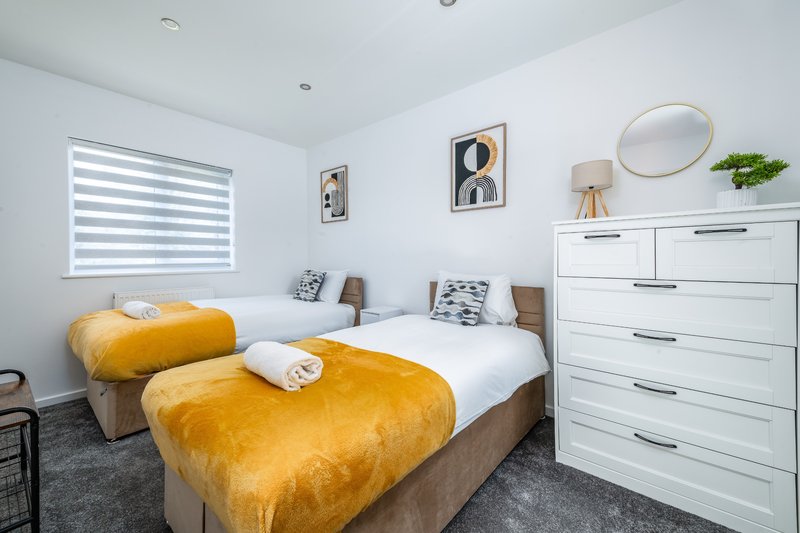 Bright bedroom with two single beds, yellow bedding, white dresser and round mirror