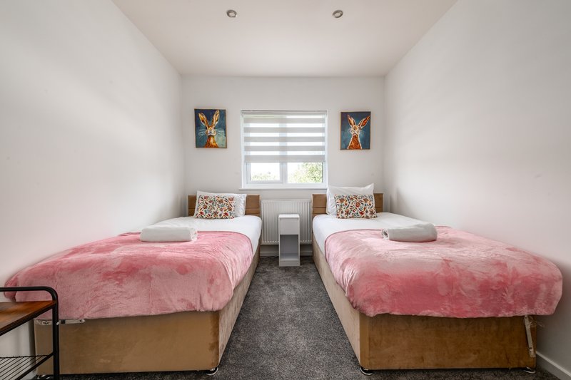 Twin bedroom with two single beds, pink bedding, wooden frames, and wall art