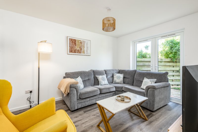 Bright living room with gray corner sofa, yellow armchair, wooden coffee table and garden doors