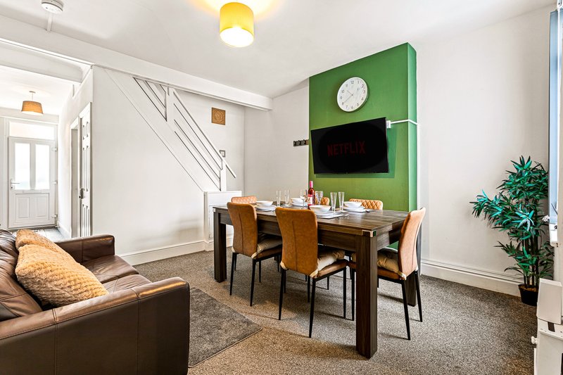 Open-plan living and dining area with leather sofa, dining table, green accent wall and wall-mounted TV